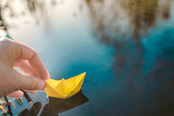 Yellow lonely floating paper boat in hand. Colorful sailing ship in big blue spring puddle, river water.Warm wet rainy weather.Hello spring,autumn.Children play,have street fun outdoors.Way to future