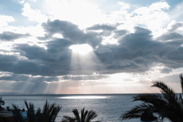 Wall Mural - Amazing cloudy sky with clouds and a beam of sun light breaking through the clouds over the ocean with palm trees. Beautiful ocean scenery