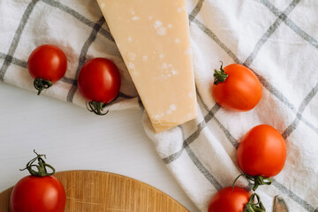 Cherry tomatoes and a piece of parmesan cheese on the table with a kitchen towel and a cutting board