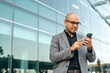 © Chanakon - Senior manager business man in suit with cell phone at the buildings downtown. Confident man using smartphone looking towards their goals for success. Executive business man
