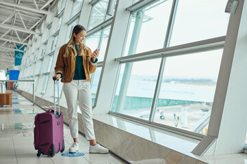 Wall Mural - Luggage, travel and woman with phone at airport for social media, web scrolling or internet browsing. Suitcase, mobile and happy female on smartphone for networking while waiting for flight departure