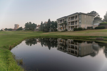 Wall Mural - Golf course with reflective pond against sky during sunset in Destin Florida. The multi-storey building with balconies is reflected in the calm water.