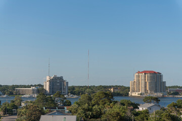 High-rise buildings and towers with waterfront in Destin, Florida. There are trees in a residential area at the front and views of tall tower in the middle of multi-storey buildings across the water.