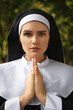 Young nun with hands clasped together praying outdoors