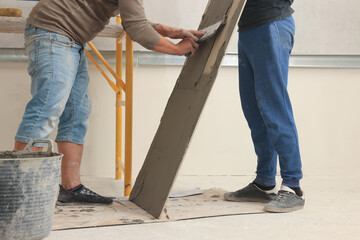 Poster - Worker spreading adhesive mix over tile with spatula, closeup