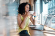 © K Davis/peopleimages.com - Window, laptop and coffee shop with a black woman blogger drinking a beverage during remote work. Internet cafe, freelance and startup with an attractive young female working in a restaurant