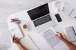 © LIGHTFIELD STUDIOS - Top view of copywriter holding pen and papers near book and gadgets on table.