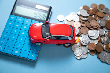 Red toy car, calculator and coins on the blue background.