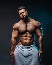 Big Muscled Man In White Towel. Handsome Hunk Posing Is Studio. Naked Male Model With Muscles And Hairy Body At Dark Background. Bodybuilder Wearing Only Bath Towel. Sexy Athlete With Six Pack Abs.