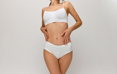 Dieting. Cropped image of slim healthy female body, breast, belly over grey studio background. Model posing in white underwear. Concept of body and skin care, fitness, natural beauty, health, wellness