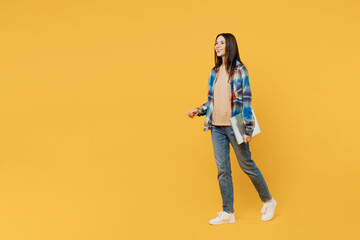 Full body side view happy young smiling IT woman wear blue shirt beige t-shirt hold closed laptop pc computer look aside isolated on plain yellow background studio portrait. People lifestyle concept.