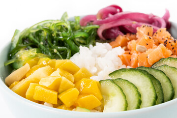 Wall Mural - Poke bowl with rice, salmon,cucumber,mango,onion,wakame salad, poppy seeds ands sunflowers seeds isolated on white background. Close up