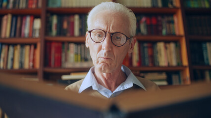 Wall Mural - Senior male researcher in eyeglasses reading an interesting book, wisdom