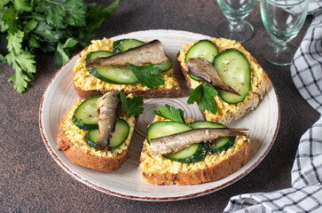 Homemade sandwiches with sprats, egg, cheese and cucumber on round plate