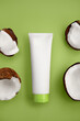 White cosmetic tube on green background. Minimal styling scene with coconut, still life. Beauty blogging, skincare