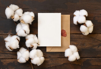 Wall Mural - Blank card and envelope with cotton flowers top view on dark brown wood, wedding mockup