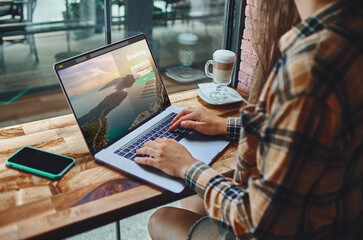 Casual smart modern woman freelancer remotely working at a laptop in a coffee shop. Cozy workplace