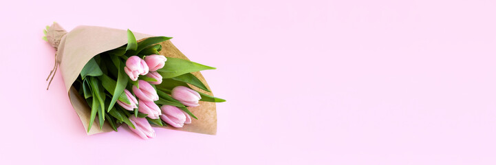 Wall Mural - Beautiful delicate bouquet of tulip flowers in craft wrapping paper on pink background banner. Panoramic web header with copy space. Wide screen wallpaper