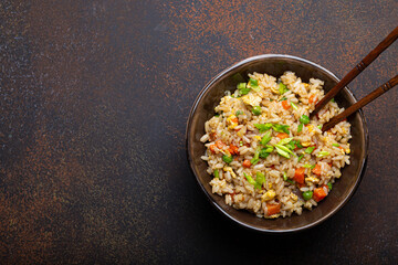 Poster - Authentic Chinese and Asian fried rice with egg and vegetables in ceramic brown bowl top view on dark rustic concrete table background. Traditional dish of China, space for text