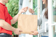 Happy smiling Asian woman receives paper bag parcel of food from courier front house. Delivery man send deliver express. online shopping, paper container, takeaway, postman, delivery service, packages