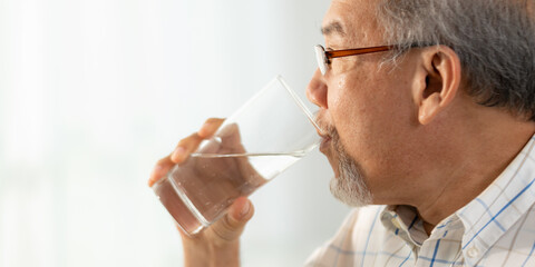 Poster - Closeup of hands of senior male and female couple holding a glass of filled clear water on table while sitting and waiting at home