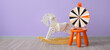 Rocking horse and stool with wheel of fortune near lilac wall in room