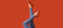 Legs Of Young Woman In Red High-heeled Shoes And Jeans Pants On Color Background