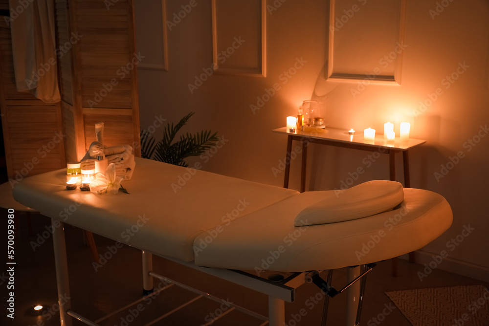 Interior of dark spa salon with couch, burning candles and table