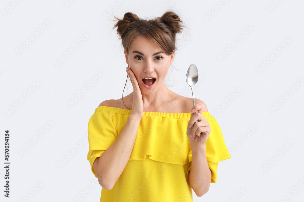 Surprised young woman with silver spoon on light background