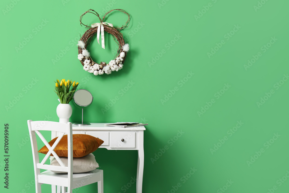 Table with tulips in vase, mirror and Easter wreath on green wall