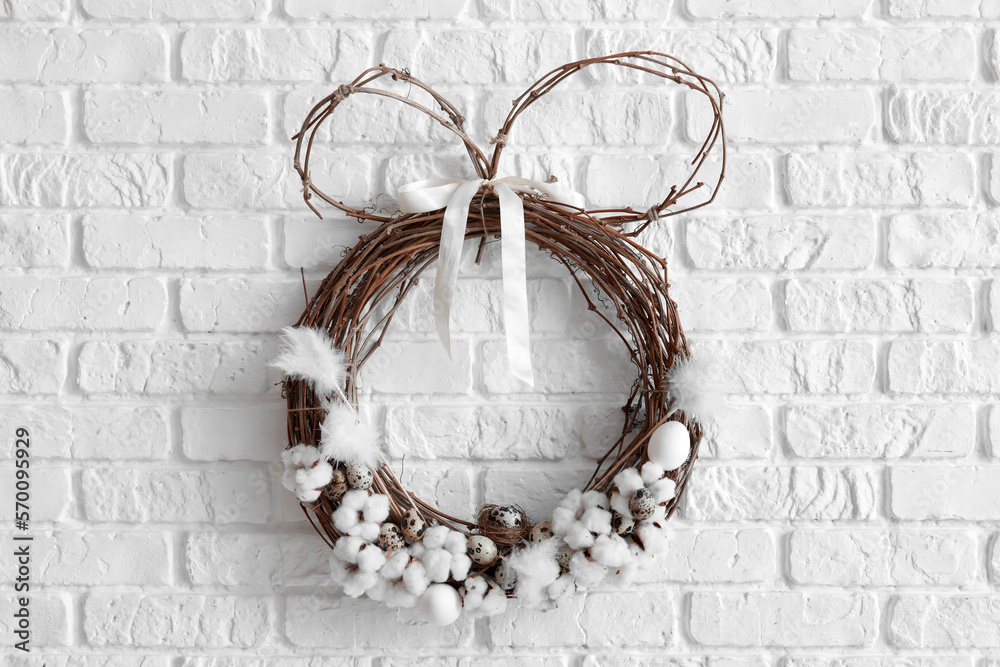 Easter wreath with cotton flowers and quail eggs on white brick wall