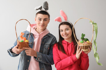 Canvas Print - Happy young couple in bunny ears with baskets of Easter eggs and rabbits on grey background