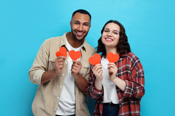 Wall Mural - Lovely couple with red paper hearts on light blue background. Valentine's day celebration