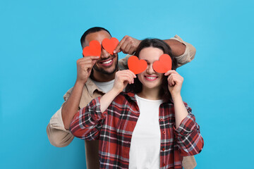 Wall Mural - Lovely couple with red paper hearts on light blue background. Valentine's day celebration