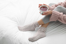 Woman With Cup Of Tea Wearing Warm Socks In Comfortable Bed, Closeup. Space For Text