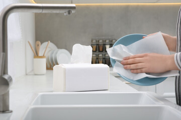 Wall Mural - Woman wiping plate with paper towel above sink in kitchen, closeup