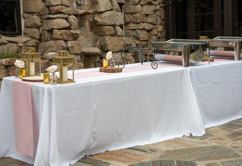 Long table setup for buffet with white table covers, pink runner, chafers and candles. Rental party equipment.