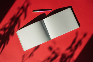 Wall Mural - A notepad with a pen lies on a colored red background. Office supplies. Place for text