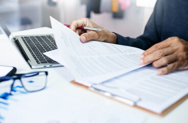 Asian businessman reviewing document reports at office workplace with computer laptop. legal expert, professional lawyer reading and checking financial documents or insurance contract