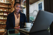 © fotofabrika - African woman having a video call on laptop while sitting in cafe.