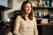 © Cavan Images - A woman professor sits at her office desk smiling with direct gaze
