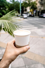 Takeaway coffee in a paper cup. A hand with a drink to go on the background of street. Paper cup mockup