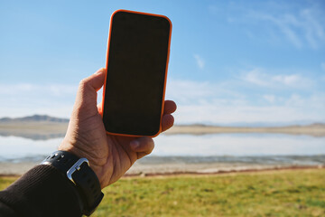 Wall Mural - Close up of mobile phone in arms of man on blurred landscape