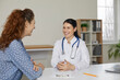 © Studio Romantic - Beautiful smiling caring female doctor having pleasant conversation with patient in medical office. Woman in white coat and with stethoscope sitting at table smiling at young female patient.