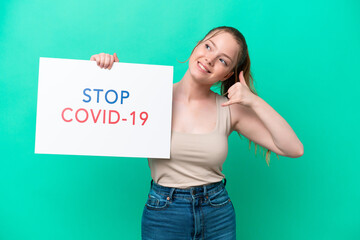 Canvas Print - Young caucasian woman isolated on green background holding a placard with text Stop Covid 19 and doing phone gesture