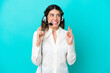 © luismolinero - Telemarketer Italian woman working with a headset isolated on blue background with fingers crossing