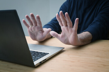 Hands in defensive gesture against a laptop computer, avoiding further work on a hacked system or other danger and offence, online risk in business and privacy, copy space,