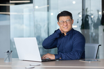 Wall Mural - Overtired office worker at work with laptop inside office, man has severe neck pain, Asian man works long time sitting