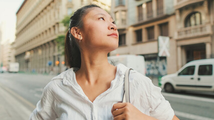 Wall Mural - Young woman using mobile phone while standing next to the road. Girl looks around