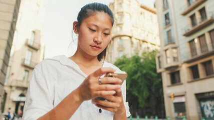 Wall Mural - Close up, young smiling woman using mobile phone while standing next to the road